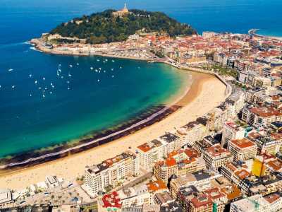 Luftaufnahme einer malerischen Küstenstadt mit goldenem Sandstrand, türkisfarbenem Wasser und einer grünen Halbinsel.