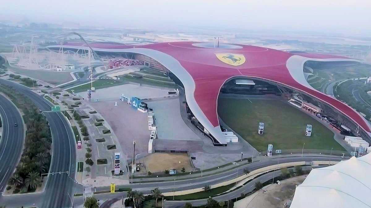 Luftaufnahme von Ferrari World Abu Dhabi, einem markanten Gebäude mit rotem Dach und Ferrari-Logo, umgeben von Straßen und Grünflächen