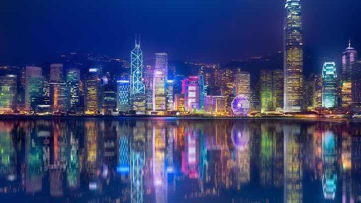 Beleuchtete Skyline von Hongkong bei Nacht mit Spiegelung im Wasser, einschließlich moderner Wolkenkratzer und dem Riesenrad.