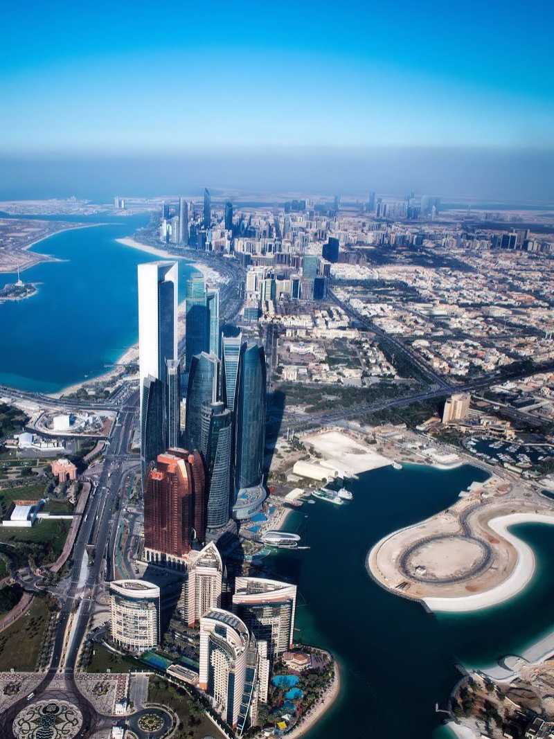 Luftaufnahme von Abu Dhabi mit den markanten Etihad Towers, modernem Stadtbild und türkisfarbenem Wasser der Küste