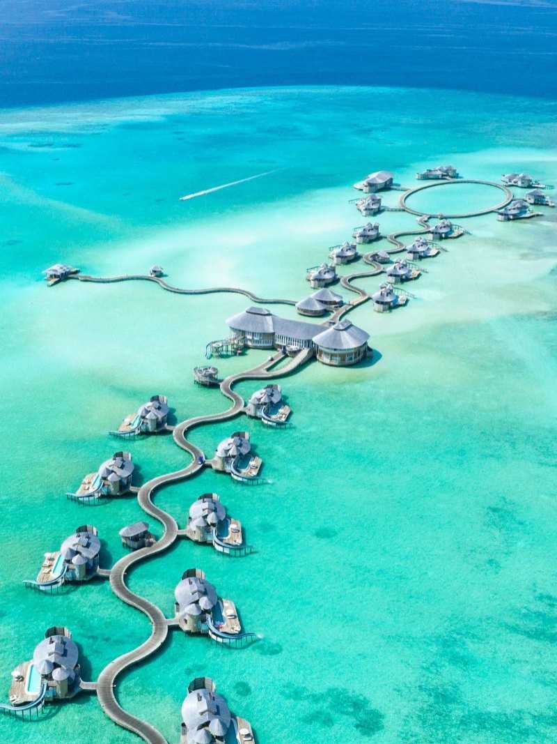 Kombireise Malediven – Exklusive Wasserbungalows im Paradies Luftaufnahme von luxuriösen Wasserbungalows auf den Malediven, verbunden durch geschwungene Holzstege über türkisfarbenem Wasser