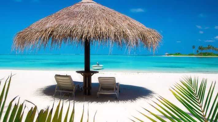 Malediven Kombi – Entspannung unter Palmen am Traumstrand Strand mit weißem Sand, zwei Liegestühlen unter einem Strohdach und türkisfarbenem Meer, umgeben von tropischen Palmen auf den Malediven