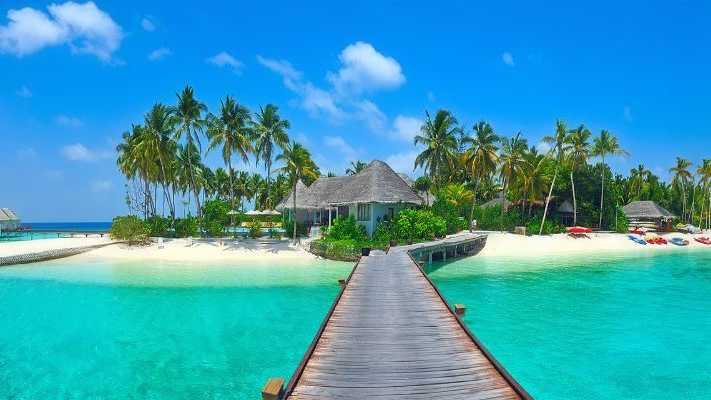 Kombireise Malediven – Exotische Inselidylle und luxuriöse Strandbungalows Türkisblaues Wasser mit Holzsteg zu einer tropischen Insel, umgeben von Palmen und Strandbungalows auf den Malediven