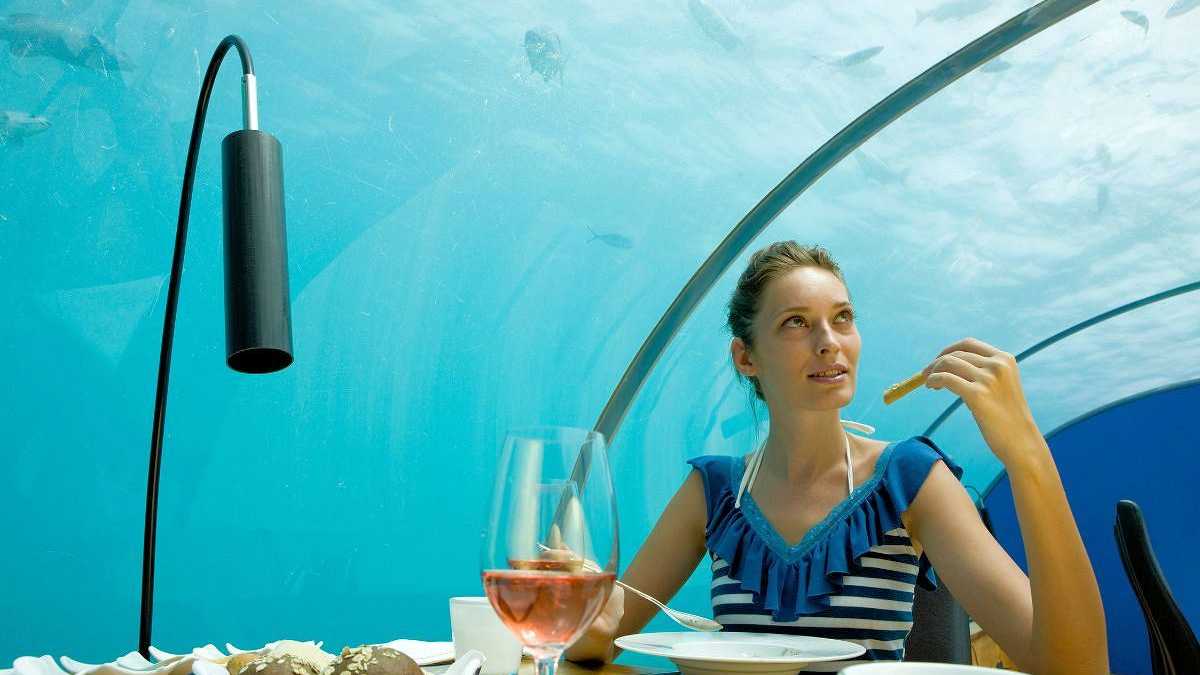 Frau speist in einem Unterwasser-Restaurant auf den Malediven mit Blick auf vorbeischwimmende Fische